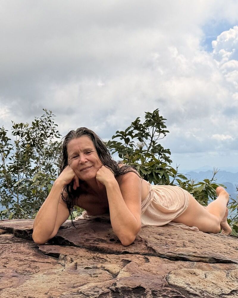 Christina liegt lachend auf einem Felsen über Krabi, hinter ihr Wolken und Grün.